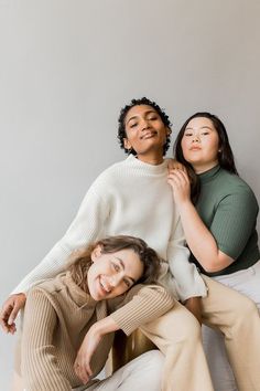 three women sitting on top of each other in front of a white wall and smiling