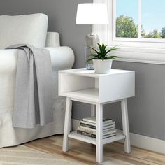 a small white table with a potted plant on it next to a couch and window