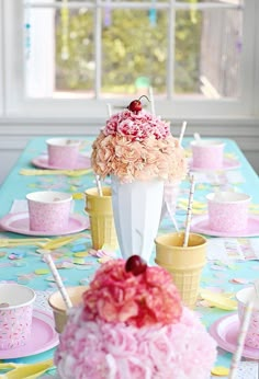 a table topped with a cake covered in flowers and ice cream cones on top of a blue table cloth