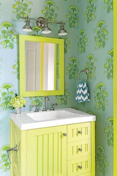 a bathroom with green and blue wallpaper, white sink and yellow vanity cabinet in front of the mirror