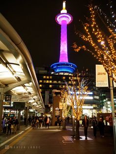 people are walking on the sidewalk in front of tall buildings with lights all around them