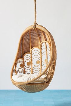 a hanging chair made out of wicker with white cushions on the bottom and sides