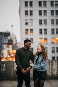 a man and woman standing next to each other in front of tall buildings at night