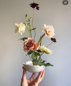 a person holding a white bowl with flowers in it and the bottom half of their hand