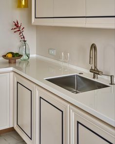 a kitchen with white cabinets and countertops has a sink, wine glass holder, and yellow lights