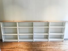 an empty white bookcase with wooden shelves on the floor in front of a wall