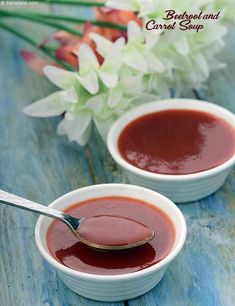 two small white bowls filled with sauce on top of a blue wooden table next to flowers