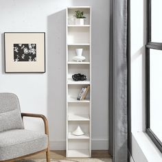 a white book shelf sitting in the corner of a living room next to a chair