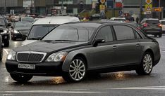 a black car driving down a street next to tall buildings and traffic lights on a rainy day