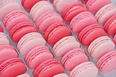 many pink and red macaroons are in a plastic container with white trim on them