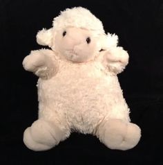 a white stuffed sheep sitting on top of a black background with its arms in the air