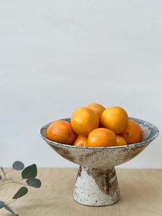 a bowl filled with oranges sitting on top of a wooden table