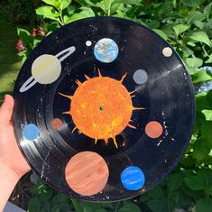 a child's hand holding a black plate with solar system on it in front of some plants