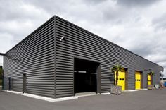 an industrial building with yellow doors and palm trees in the front yard on a cloudy day