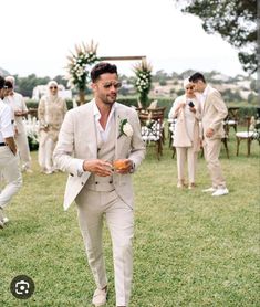 a man in a suit and tie walking through the grass with other people behind him