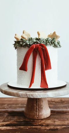 a white cake with red ribbon and bow on top, sitting on a wooden table