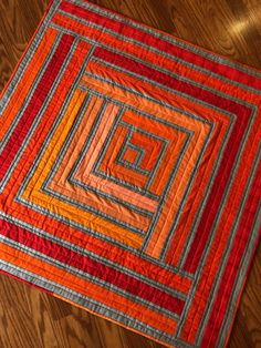 an orange and red quilt on a wooden floor