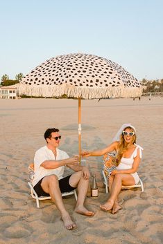 a man and woman sitting under an umbrella on the beach