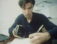 a man sitting at a desk with a camera in his hand and writing on a piece of paper