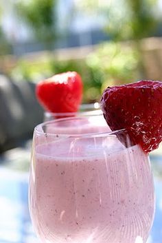 two strawberries sit on top of a smoothie in a wine glass with another one behind it