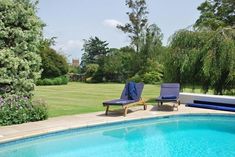 two lawn chairs sitting next to a swimming pool in a backyard with grass and trees