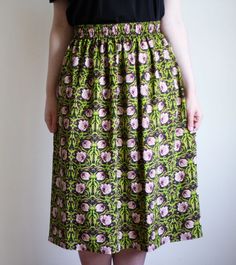 a woman wearing a black top and green floral print skirt with her hands in her pockets