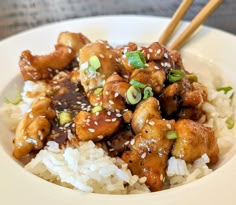 a white bowl filled with rice and chicken covered in sesame seeds on top of it