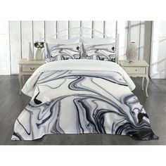 a white bed with black and grey marble print on it, along with two nightstands