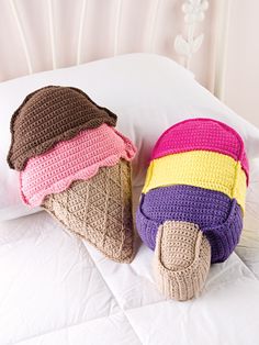 two crocheted ice cream cones are laying on a bed with white sheets and pillows