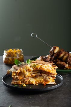 a stack of food sitting on top of a black plate next to another plate filled with food