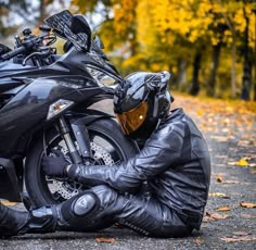 a man sitting on the ground next to a motorcycle wearing a black leather outfit and helmet