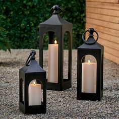 three black lanterns sitting on top of a gravel ground