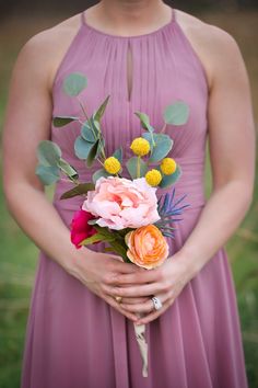 a woman in a purple dress holding a bouquet of flowers and greenery with her hands