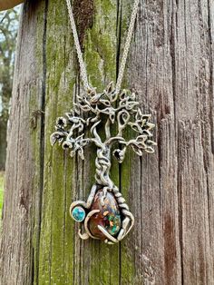 "The roots of this Primeval Forest Tree Pendants encircle a beautiful Australian Boulder Opal. Intricate leaves crown the tree. The pendant is cast in sterling silver and measures 2.5\" tall and just over 1.5\" wide (63.5 x 38 mm). Each Primeval Forest Tree is a unique piece in Alisha's limited edition collection. Primeval Forest Tree # 19 features an Australian Koroit Boulder Opal with radiant aqua blues and greens contrasting against an earthy orangey-red, and with a 4mm Blue Topaz which sparkles in the cradle of the twisting root This is one of a limited edition of 50. Each one will differ slightly with the roots entwining various gemstones. All Marty Magic Jewelry is packaged in a beautiful box, embossed with the gold foil Marty Magic dragon logo. Perfect for any occasion! Designed in Unique Tree Of Life Round Jewelry, Leaves Crown, Opal Gifts, Leaf Crown, Tree Jewelry, Tree Lover, Jewelry Opal, Australian Boulder Opal, Tree Hugger