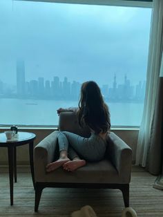 a woman is sitting in a chair looking out the window at the cityscape