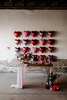 a table topped with lots of heart shaped balloons next to a wall filled with candles