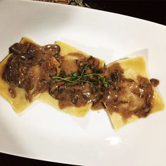 a white plate topped with ravioli covered in gravy and mushroom toppings