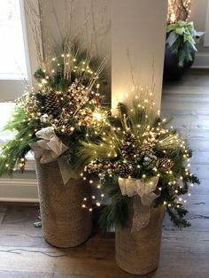 two vases filled with pine cones and evergreen branches are adorned with lights, bows and twine