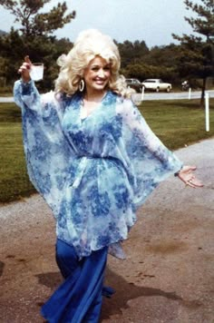 a woman is walking down a path with her hand in the air while wearing a blue dress