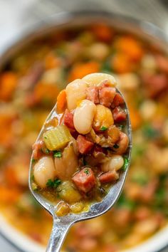 a spoon full of soup with beans and carrots on the top is held up