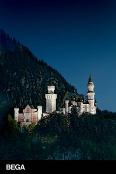 an old castle on top of a hill with trees in the foreground and dark blue sky above