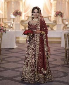 a woman in a red and gold bridal gown holding a bouquet of flowers on her wedding day