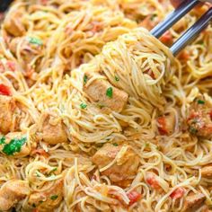 someone is holding chopsticks over some noodles with meat and vegetables in it on a plate