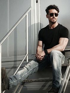 a man sitting on top of a metal hand rail next to a stair case with his legs crossed