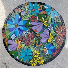 a glass plate with colorful flowers on it sitting on the ground next to a sidewalk