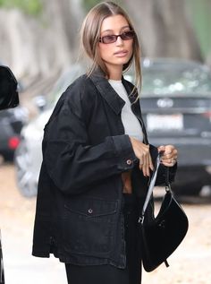 a woman in black jacket and leggings walking down the street with her hand on her hip