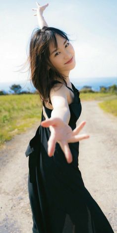 a woman in black dress standing on dirt road with her arms out and hands outstretched