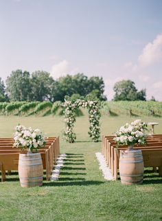 an outdoor ceremony set up with wooden barrels and white flowers on the aisle, surrounded by greenery