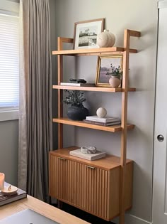 a wooden shelf with pictures on it next to a window in a living room area