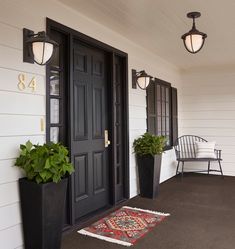 two planters are on the front porch of a house with black doors and windows